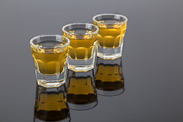 three shots of tequila gold on the dark mirror surface