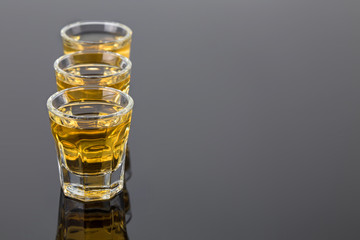 three shots of tequila gold on the dark mirror surface