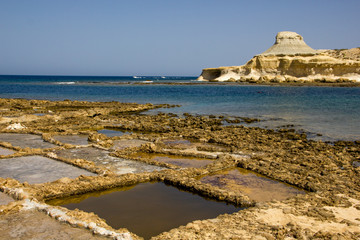Farming salt in salt fields or salt pans in Gozo with the distinguished view on the little hill in...