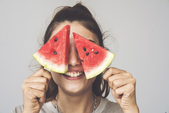 Young woman holding watermelon slices popsicles on her eyes