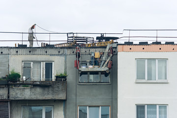 Works on plaster facade. The workers have finished their part of the work and one of them picks up the cradle upstairs to his colleague, who understands the ropes and fastenings on the roof 