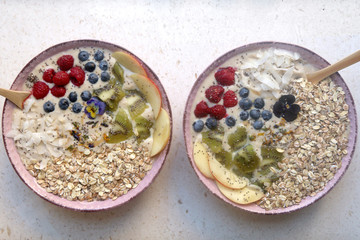 Two healthy smoothie bowls. Mango, peach and banana smoothie with various toppings (granola, coconut flakes, chia seeds, kiwi, blueberries, raspberries, peach). Top view. 
