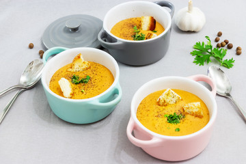 Three small serving pots or bowls with cream soup made of red lentils with rusks, spices and herbs parsley, coriander. Light gray background.