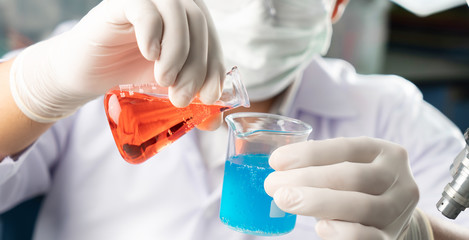 Chemist student boy pouring blue liquid in beger glass to erlenmeyer flask chemistry with red liquid on biochemical experiment. Mix water in laboratory.