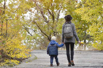 Obraz premium Mom and son are walking in the autumn forest. Back view