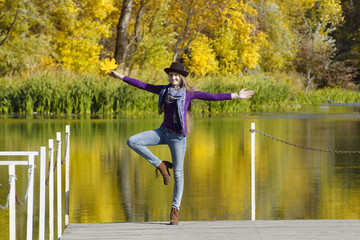 Fototapeta na wymiar Funny young woman in the hat is standing on the pier. Autumn sunny day. Back view