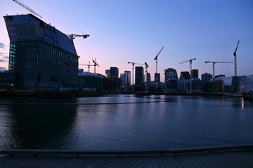 Fototapeta premium Background of silhouette skyscrapers and cranes under construction. Industrial city landscape at night, Bjorvika, Oslo, Norway.