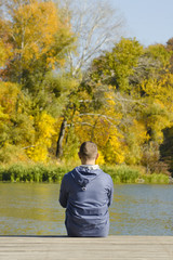 Fototapeta premium Young man sits on the pier. Autumn sunny day. Back view