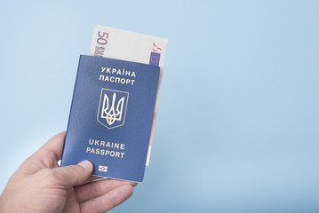 Ukrainian passport and euro cash in the man's hand. Travel concept. Blue background