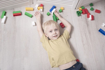 Naklejka premium Blond boy lies on the floor among the designer. Top view