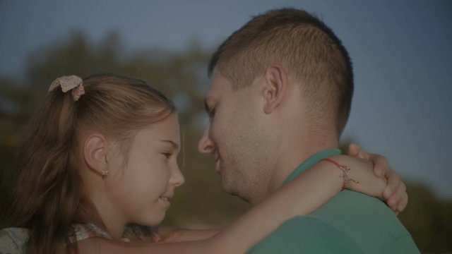 Portrait of affectionate handsome dad and daughter embracing and kissing while standing face to face outdoors. Caring father expressing his feelings to lovely laughing girl. Close-up.