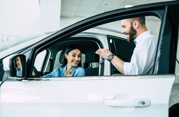 Gift for darling. Happy young couple chooses and buying a new car for the family in the dealership.