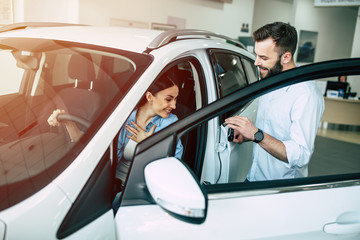 Beautiful young modern couple chooses and buying a new car for the family in the dealership. Woman inside of car tests it