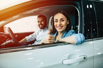 Happy beautiful young couple chooses and buying a new car for the family in the dealership while sitting inside one of car.