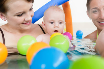 Fototapeta na wymiar Mothers and their kids having fun at baby swimming lesson between lots of water balls