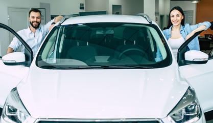 Happy young lovely couple in casual wear buying first new family car together in dealership.