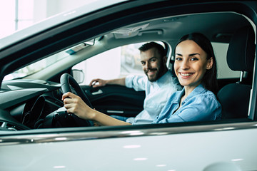 Happy beautiful young couple chooses and buying a new car for the family in the dealership while...