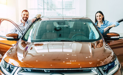 Happy young couple chooses and buying a new car for the family in the dealership.