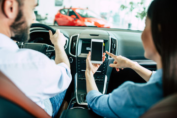 Back view of young Lover couple in car, man driving in city and woman using navigation on mobile...