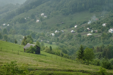 Wooden barn located on the slope of the hill, covered with forest and meadows. Ecology concept of clean environment. Natural background. Taken at misty spring day at Carpathian mountains, Ukraine.