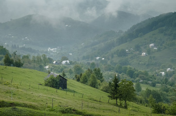 Wooden barn located on the slope of the hill, covered with forest and meadows. Ecology concept of clean environment. Natural background. Taken at misty spring day at Carpathian mountains, Ukraine.