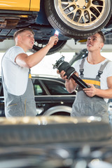 Two skilled auto mechanics analyzing together the rims of a lifted car while working in a modern...