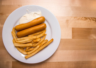Sausages and French fries with sauce placed on wooden table.
