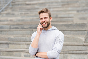 Keep in touch. Man bearded walks with smartphone, urban background with stairs. Man pleasant smiling face speaks on smartphone. Guy pleased answer call on smartphone. Pleasant conversation