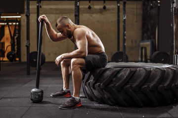 handsome bodybuilder with closed eyes is resting after doing sledgehammer exercises at the gym. full length side view photo
