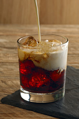 Pouring cream into cocktail White Russian. Vodka, coffee liquor, cream and ice