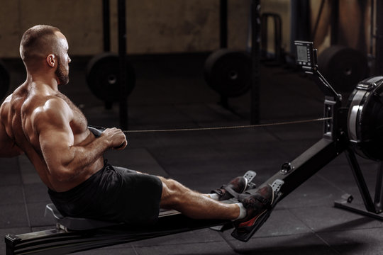 Full Length Side View Shot. A Fit Young Man Working Out With A Indoor Rower. Lifestyle And Hobby Concept