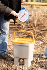 Person weighting a bucket with a weigh scale for composting  