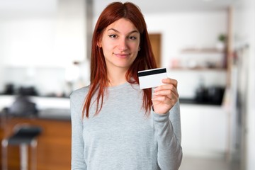 Fototapeta na wymiar Young redhead girl holding a credit card on unfocused background