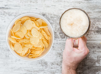 man's hand holds a beer near chips. Top view