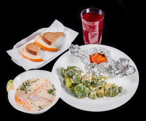 Delicious dinner table with baked meat and broccoli, fish soup with salmon and prawn, bread and compote on black background .
