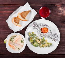 Delicious dinner table with baked meat and broccoli, fish soup with salmon and prawn, bread and compote on wooden background.