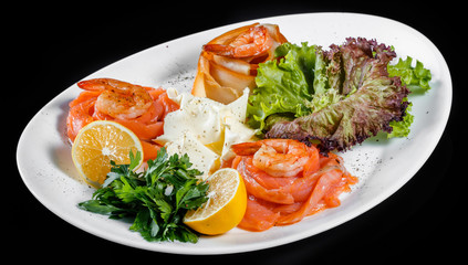 Seafood platter with salmon slice, pangasius fish, shrimp, decorated with lemon and greens on black background isolated