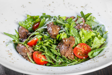 Hot salad with fried liver, cherry tomatoes and mixed greens on dark wooden background. Healthy food. Ingredients on table