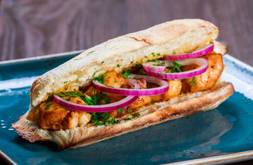 Grilled chicken in sandwich from fresh pita bread with onion and greens on dark wooden background....