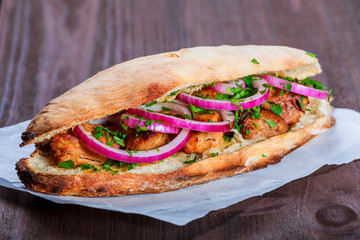 Grilled chicken in sandwich from fresh pita bread with onion and greens on dark wooden background....
