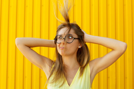 Portrait of a joyful girl wearing toy funny glasses blowing away her hair from face over yellow background at daylight