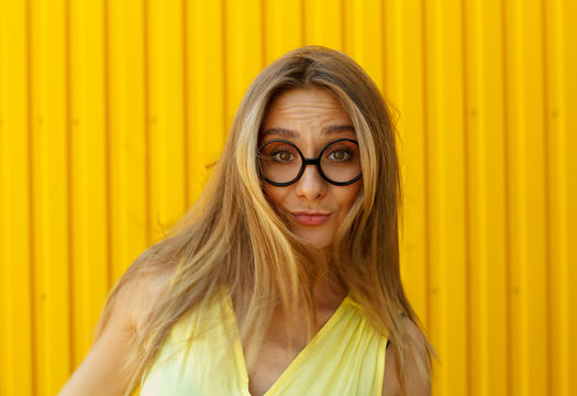 Portrait of a joyful girl wearing toy funny glasses over yellow background at daylight