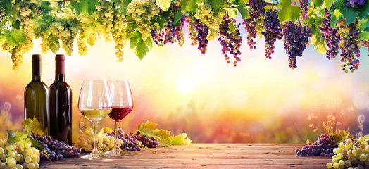 Fotobehang Flessen en wijnglazen met druiven bij zonsondergang © Romolo Tavani