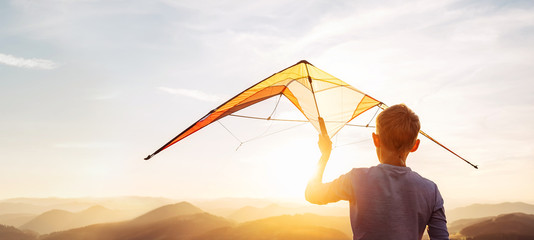 Boy prepare start to fly a kite over the sunset mountain hills