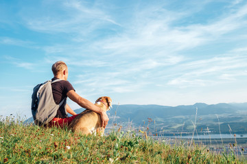 Fototapeta na wymiar Man with his beagle dog sits on the top of hill over the mountain valley