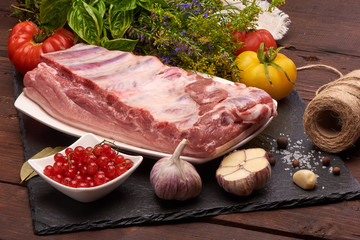 Raw pork meat on a slate stone plate with spices, colorful tomatoes and red currant on a wooden rustic background.