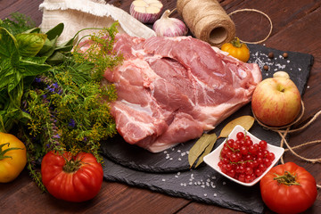 Raw pork meat on a slate stone plate with spices, colorful tomatoes and red currant on a wooden rustic background.