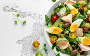 Healthy Nicoise salad with salmon, colourful sweet cherry tomatoes, olives, green beans, cucumber ribbons, soft boiled eggs, water-cress leaves with Mediterranean seasoning