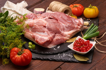 Raw pork meat on a slate stone plate with spices, colorful tomatoes and red currant on a wooden rustic background.