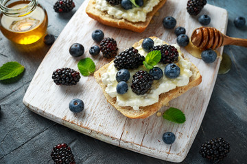 Fresh sweet Blackberry, Blueberry bruschetta, toast with cottage cheese, honey in a white board.